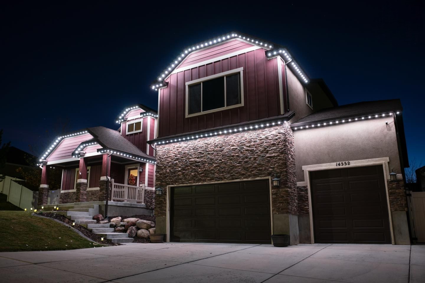 Warm white permanent roofline lighting on a red and stone home at dusk